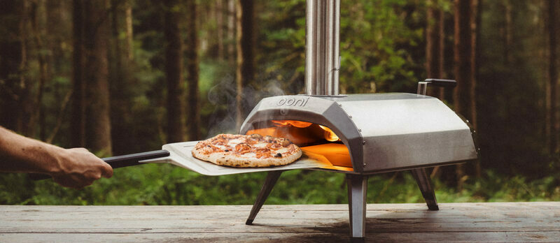 Hand putting pizza into an Ooni pizza oven on spatula.