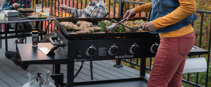 Woman grilling chicken and vegetables on a Blackstone griddle.